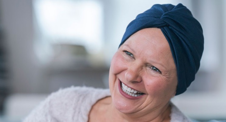 A woman wearing a head covering smiles brightly. Her expression conveys strength, hope, and resilience in the face of adversity.