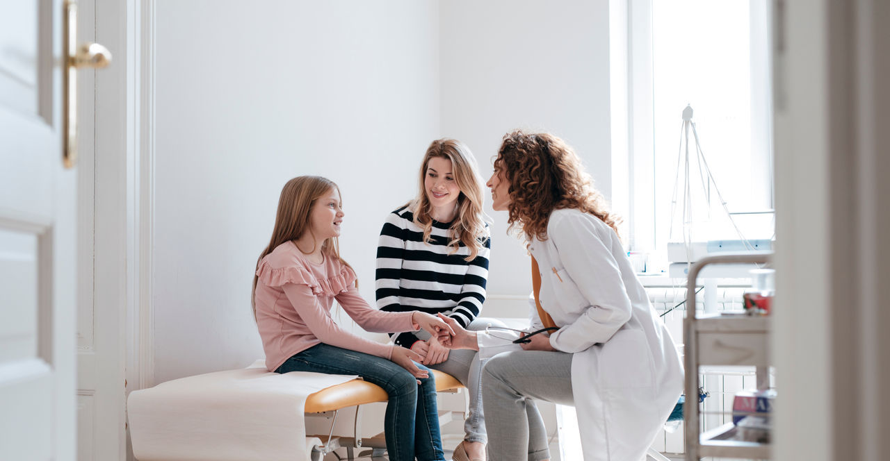 Cute Caucasian girl and her mother talking with a doctor at exam.