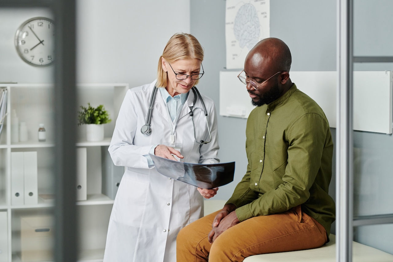 Confident mature doctor in whitecoat showing young black man x-ray image of his lungs and explaining him diagnosis in clinics